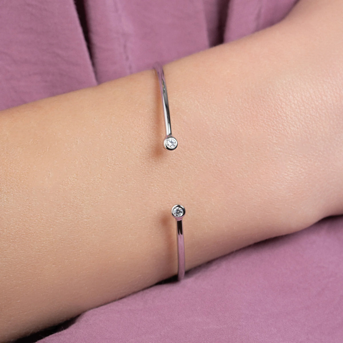Bracelet jonc ouvert et deux zircons sertis clos en argent 925 porté au poignet, gros plan sur une manche violette