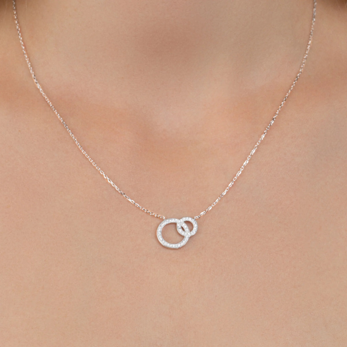 Collier deux anneaux entrelacés dont un pavé de zircons en argent 925, porté au cou