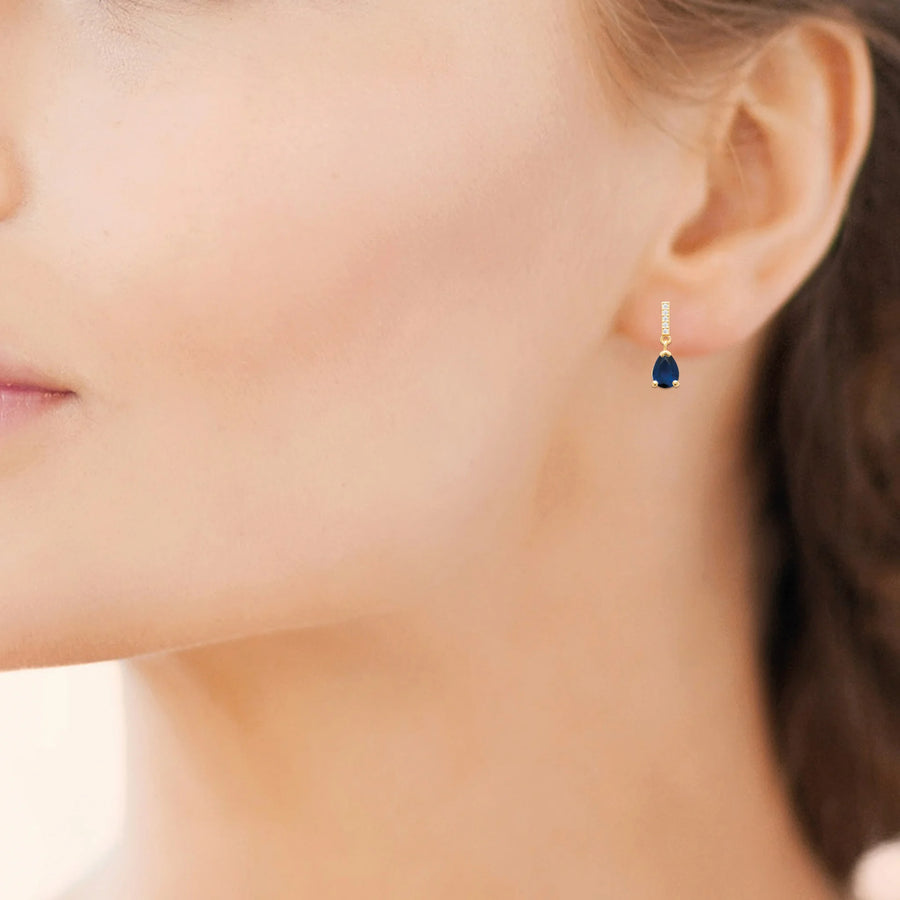 Boucles d’oreilles pendantes barrette de zircons et goutte bleu nuit en plaqué or, portées à l’oreille