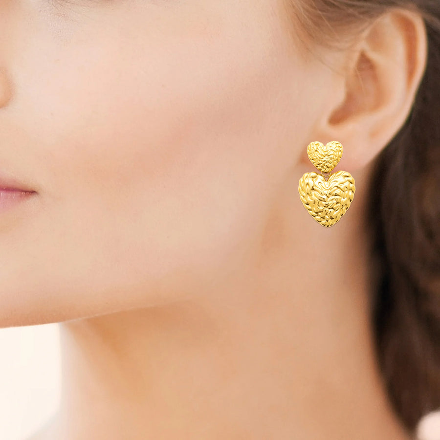 Boucles d’oreilles pendantes deux cœurs martelés en acier PVD doré, portées à l’oreille