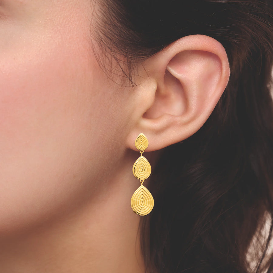 Boucles d’oreilles pendantes trois gouttes guillochées en acier PVD doré, portées à l’oreille
