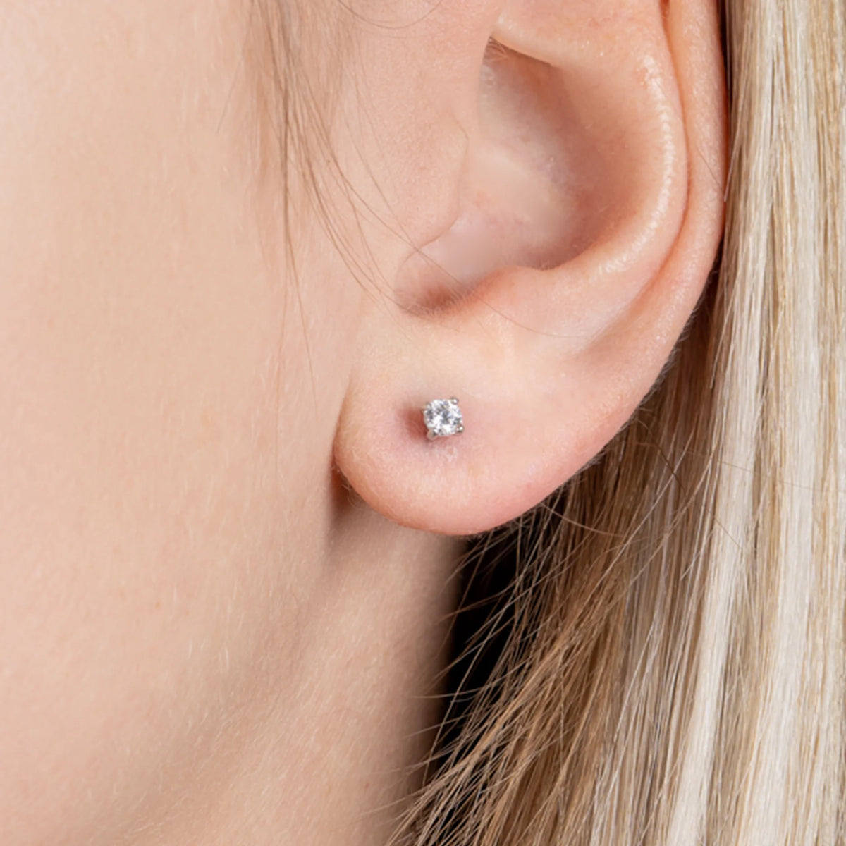 Boucles d’oreilles puces solitaire zircon quatre griffes en argent 925, portées par une femme