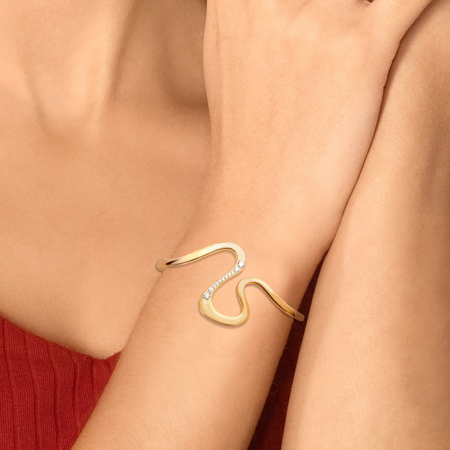 Bracelet jonc ouvert sinueux et zircons en plaqué or, porté au poignet