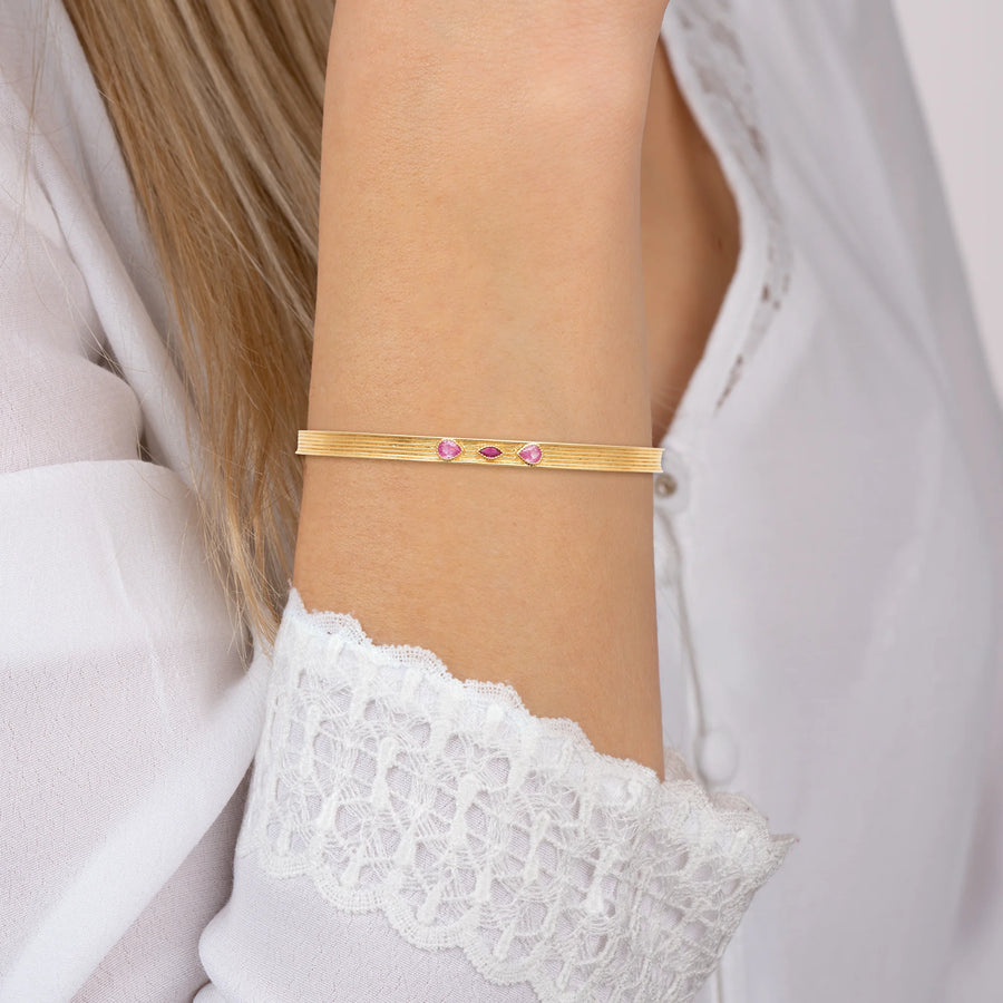Bracelet jonc ouvert strié et trois pierres roses en plaqué or, porté au poignet