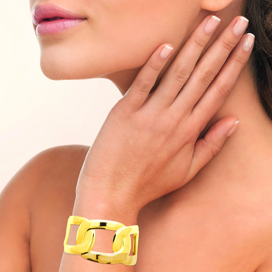 Bracelet manchette ouverte à larges maillons ajourés en acier PVD doré, porté au poignet