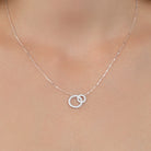 Collier deux anneaux entrelacés dont un pavé de zircons en argent 925, porté au cou