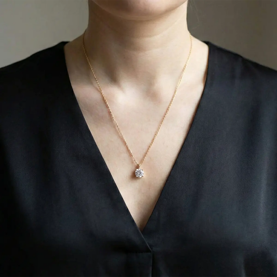 Collier à pendentif porté dans un décolleté en V sur un chemisier noir