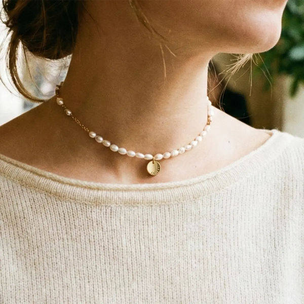 Collier ras de cou de perles porté à la base du cou sur un pull crème
