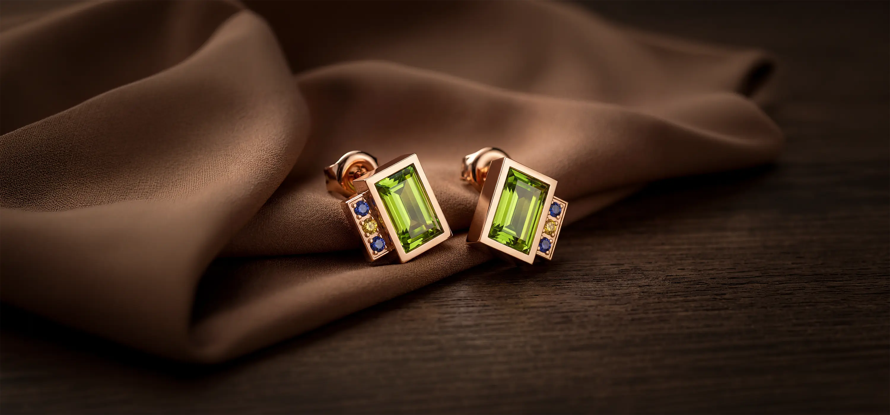 Gros plan sur une paire de boucles d'oreilles Art Déco en or rose 18k, serties d'un péridot central taille émeraude et de pierres fines colorées, illustrant l'élégance solaire de la collection Bijoux Péridot Bajoia