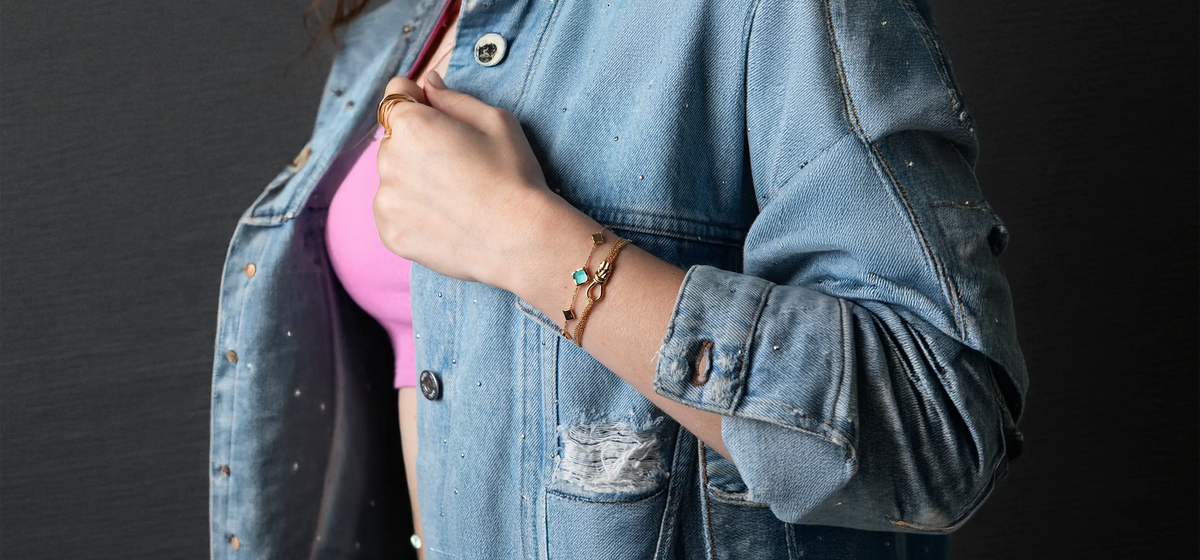 Poignet de femme portant une accumulation de bracelets fantaisie Bajoia, joncs dorés et chaînes fines